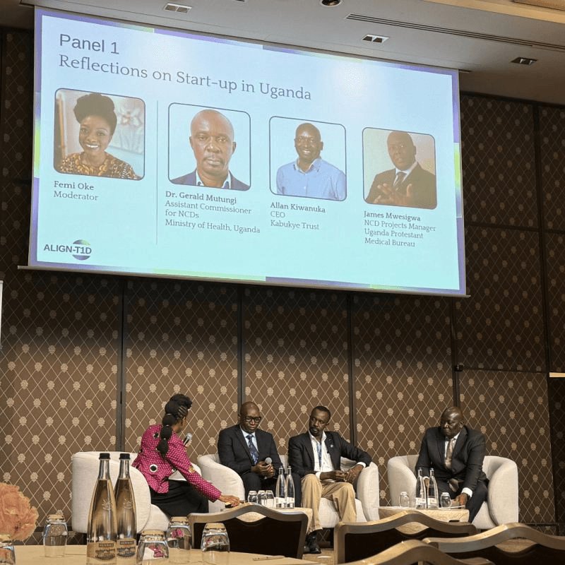 Panel 1 — "Reflections on Start-up in Uganda" — at the ALIGN-T1D event on the sidelines of WHA79 in Geneva. From left: moderator Femi Oke; Dr Gerald Mutungi of Uganda's Ministry of Health; Allan Kiwanuka, CEO of Kabukye Trust; and James Mwesigwa of the Uganda Protestant Medical Bureau.